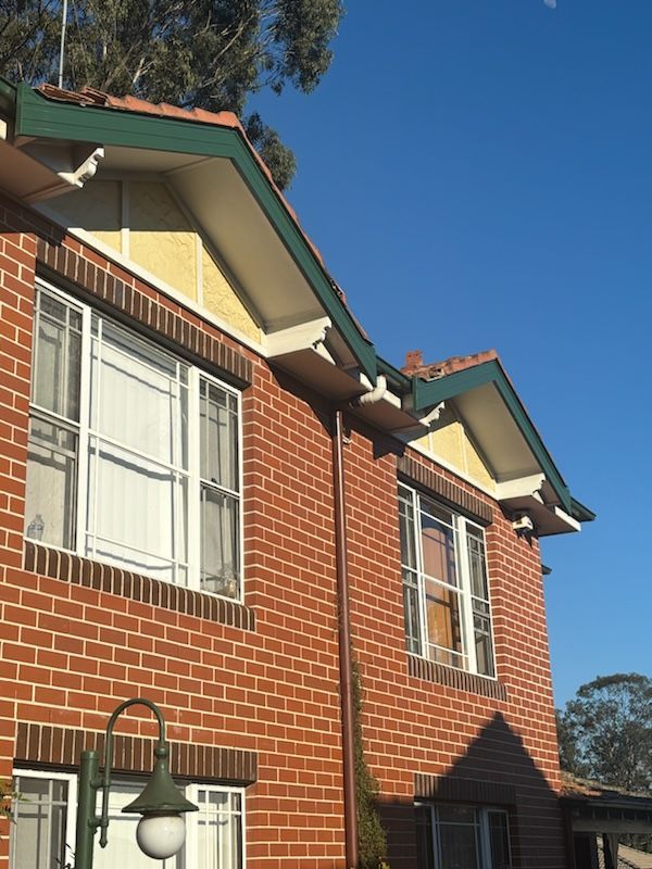 Red brick building with green roof trim and white window frames against a blue sky.