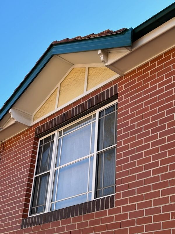 Brick building with a window, triangular window above. Blue sky.