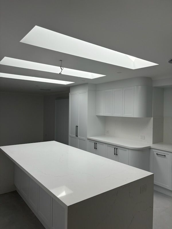 White kitchen with large island and skylights in the ceiling. Cabinets and countertop are white.