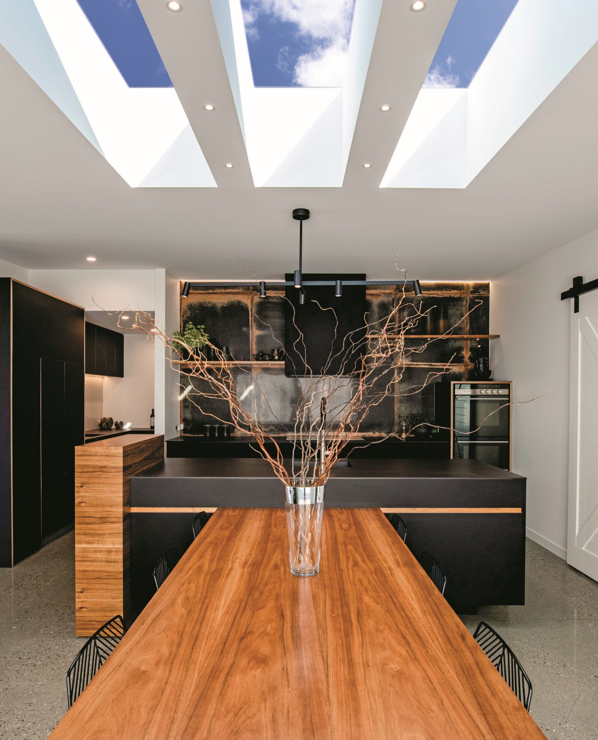 Modern kitchen with a long wood table, black cabinets, and skylights.
