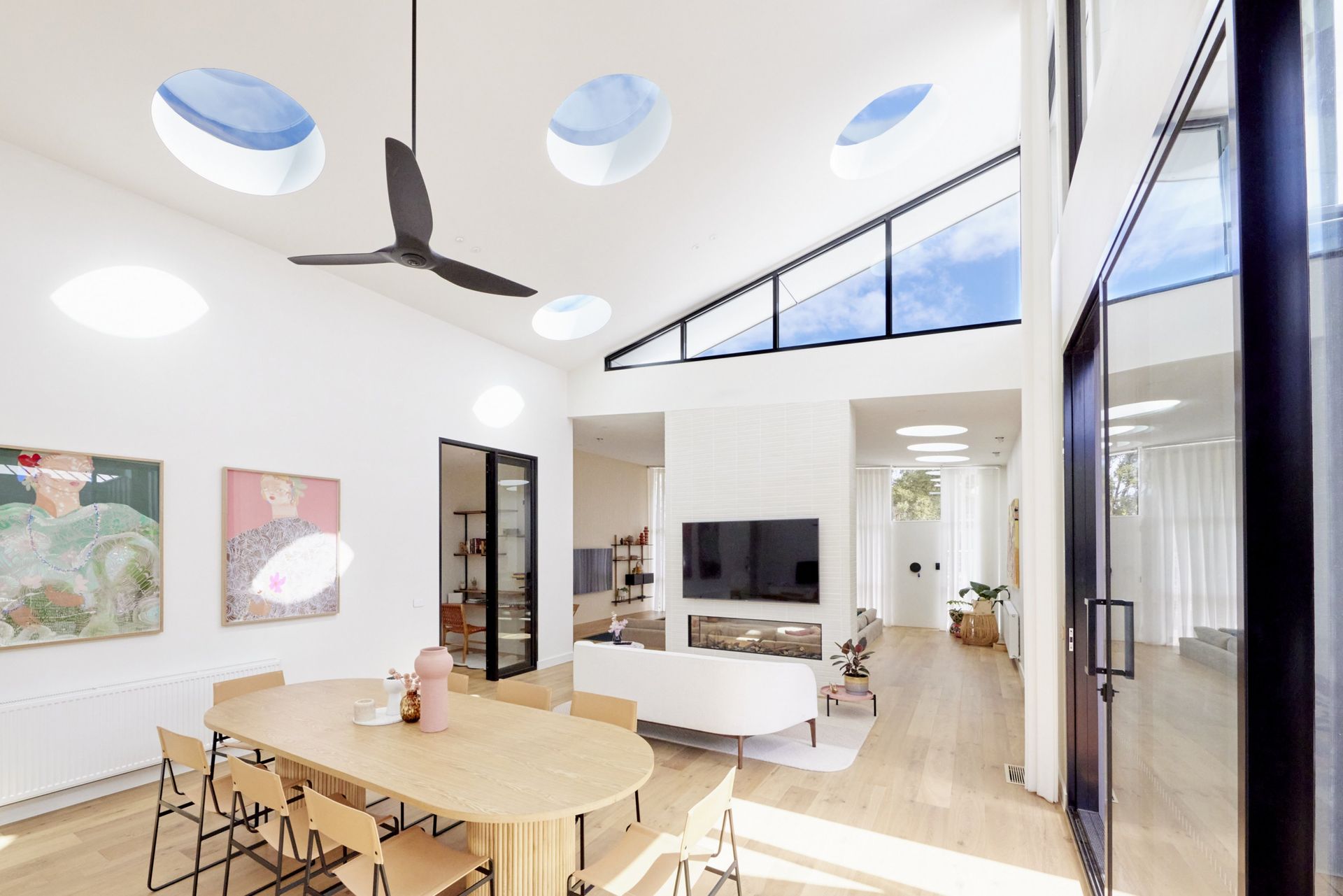 Bright, modern living room with skylights, a dining table, and a view to the outside.