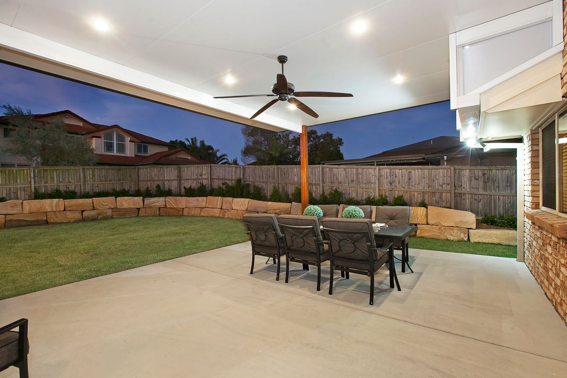 Outdoor patio with table and chairs, beneath a covered ceiling. Backyard, night.