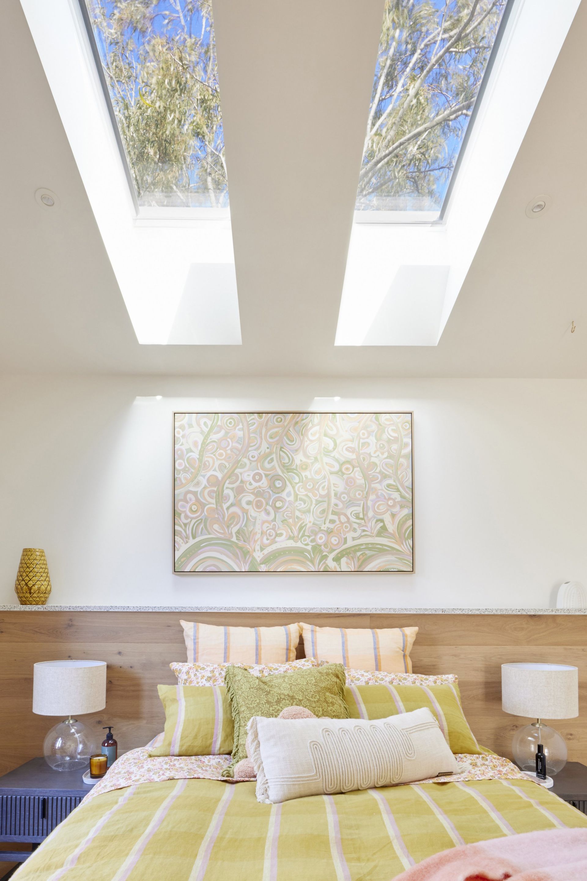 Bedroom with skylights, bed, and artwork; light and airy with yellow and neutral tones.