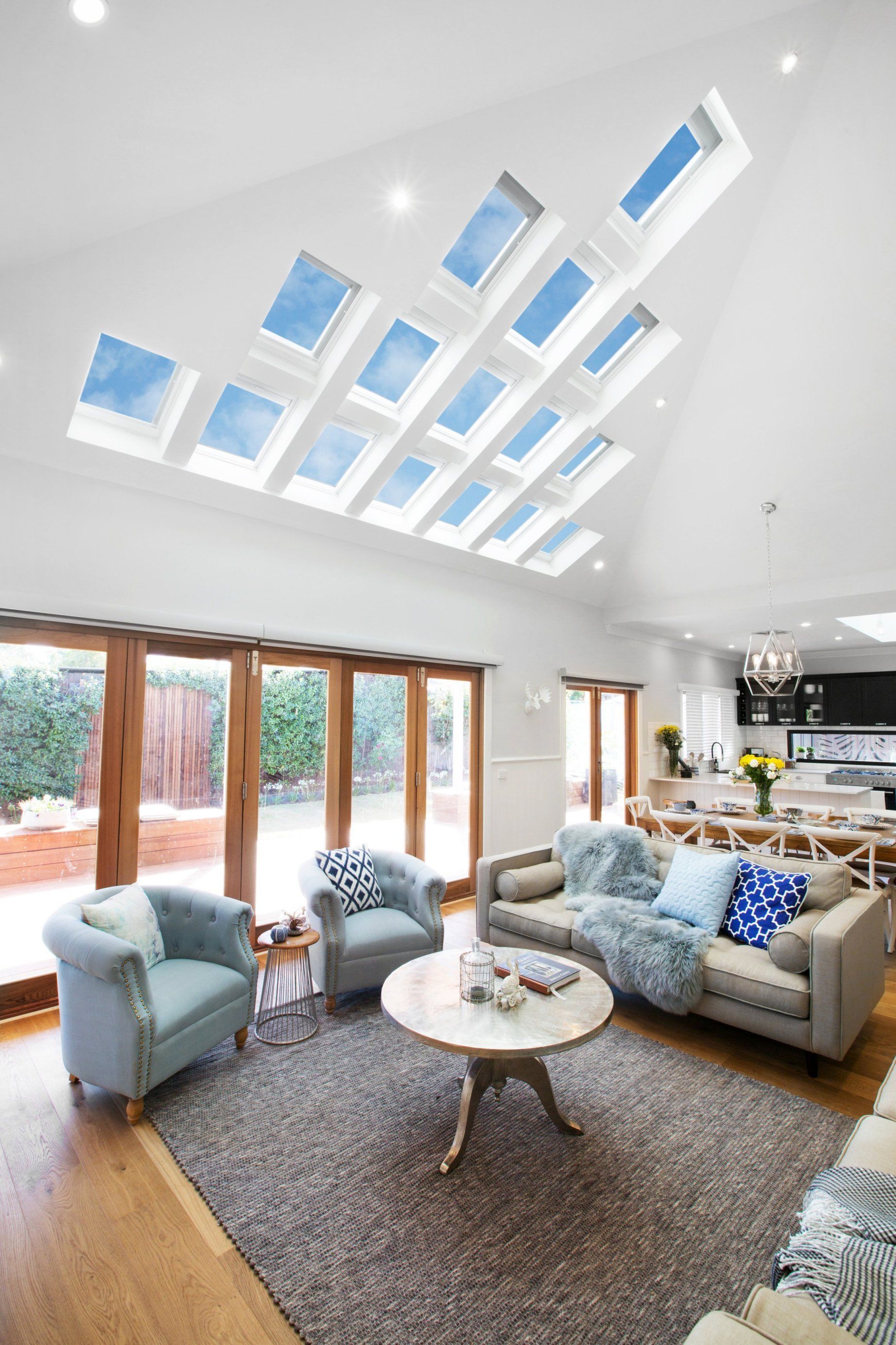 Living room with blue armchairs, tan sofa, skylights, and wooden-framed glass doors, light wood floors.