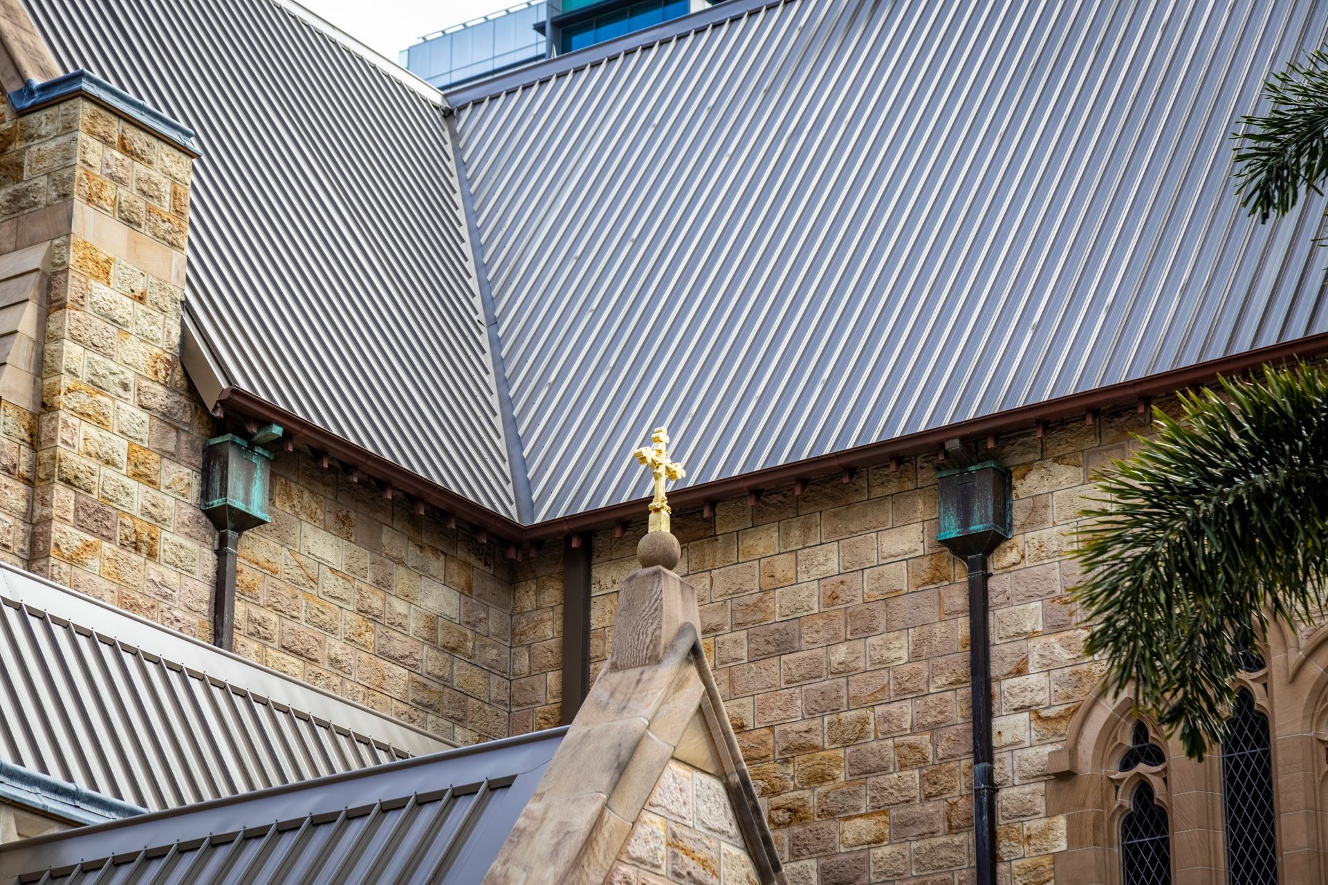 Exterior of a stone church with a corrugated metal roof. A golden cross sits atop the building.