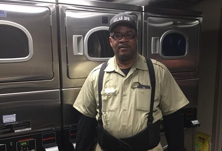 A man is standing in front of a stack of washing machines in a laundromat.