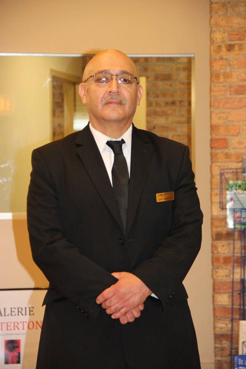 A man in a suit and tie stands in front of a sign that says galerie terton