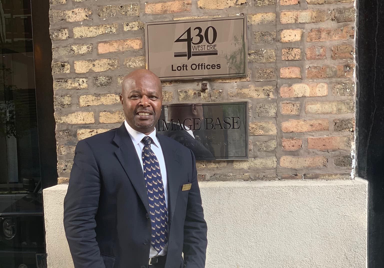 A man in a suit and tie is standing in front of a brick building.