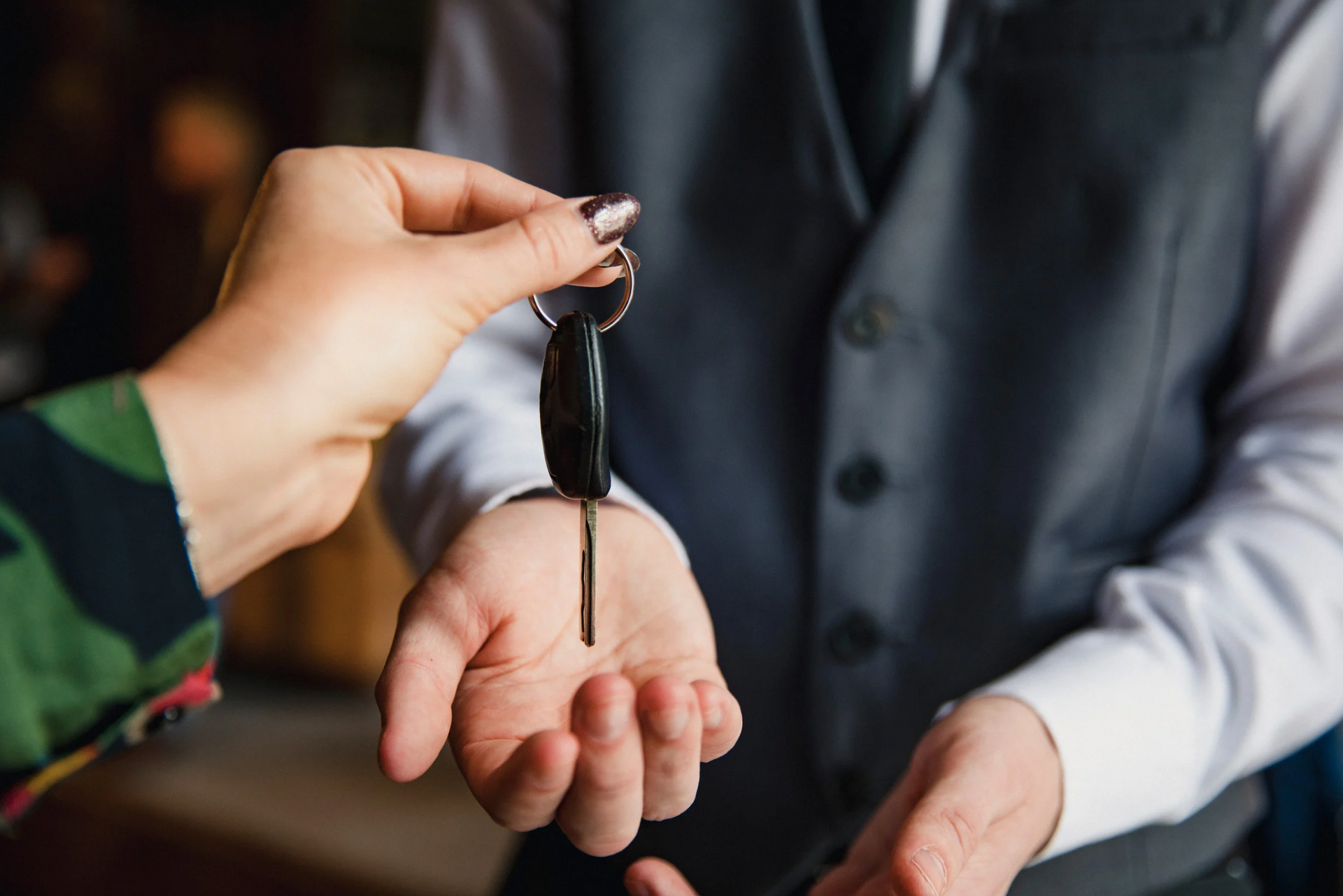 A woman is handing a car key to a man in a suit.