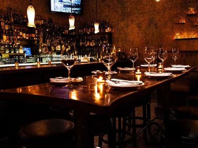 Dimly lit bar with set wine glasses and plates on a polished wooden table