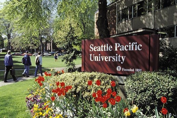 Seattle Pacific University sign beside flowerbed and people walking on campus lawn