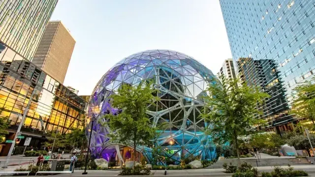 Glass geodesic dome in a modern plaza, surrounded by trees and tall office buildings at dusk