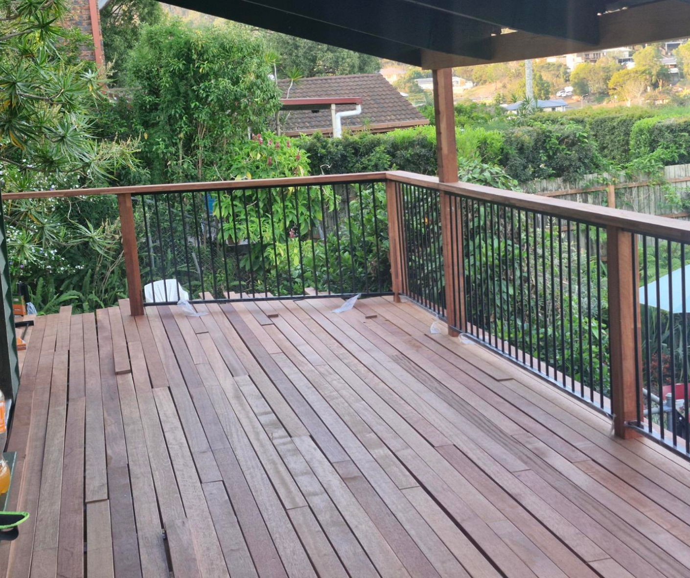 Wooden deck patio with black metal railing, overlooking a garden and neighboring houses.