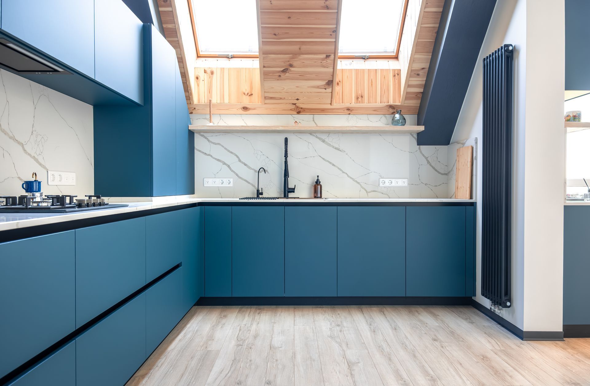 Blue modern kitchen with skylights, light wood floors, and white marble backsplash.
