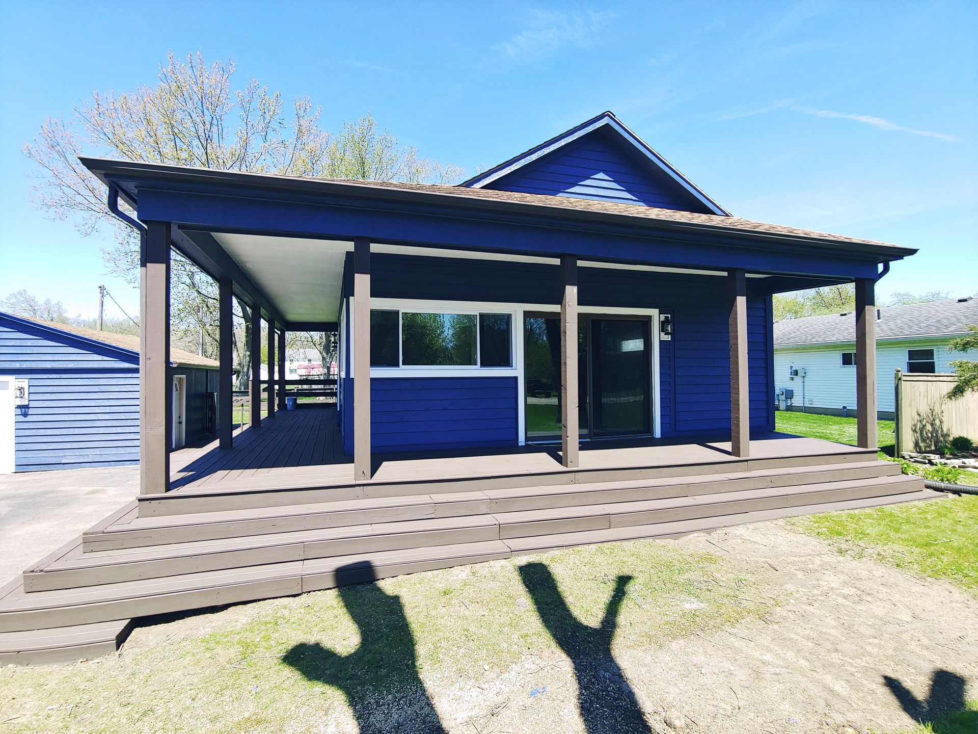 A deep blue house with a dark brown, multi-level deck and porch, set against a clear blue sky on a sunny day.