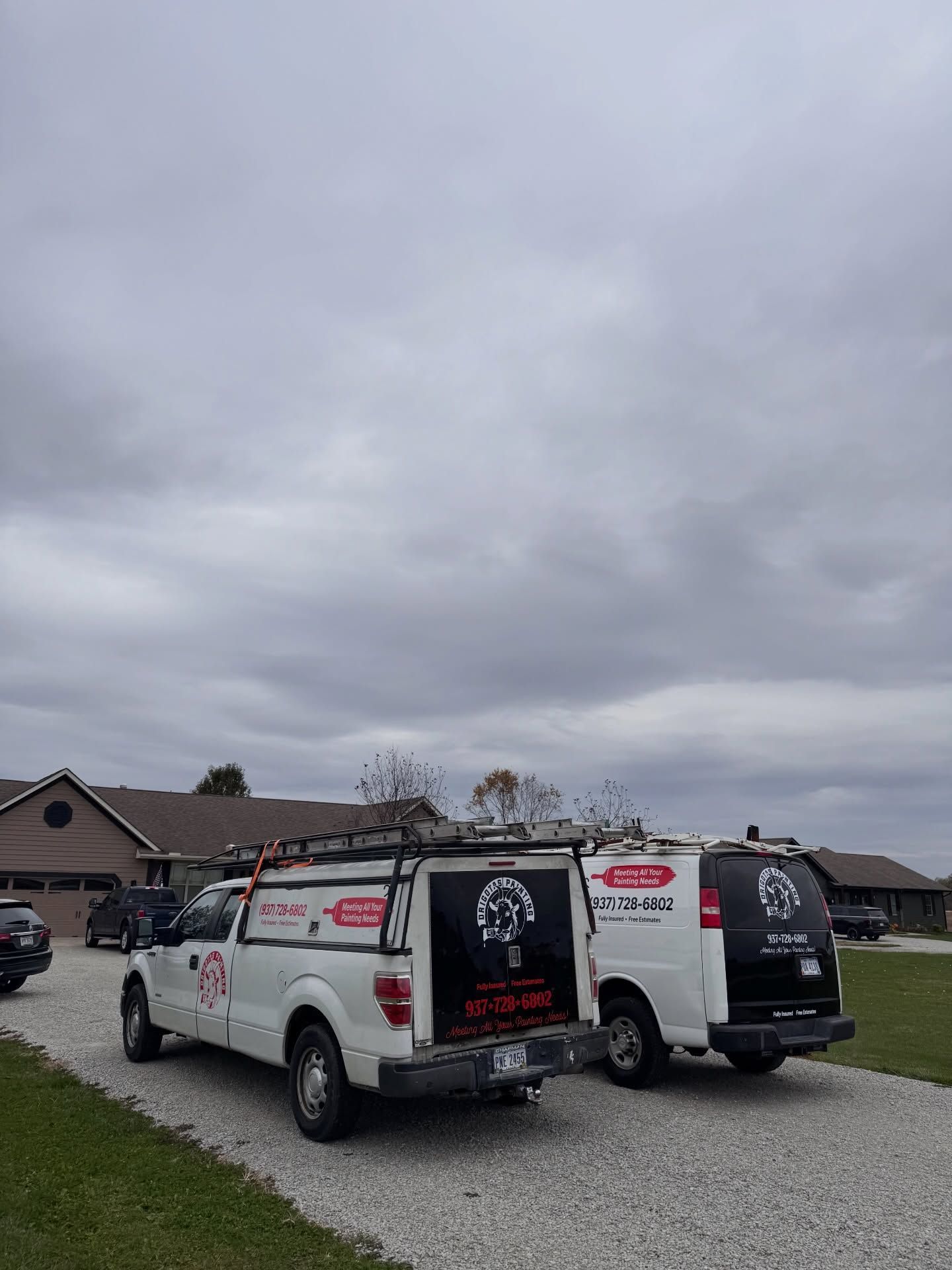 White work trucks parked in front of a house under a cloudy sky.