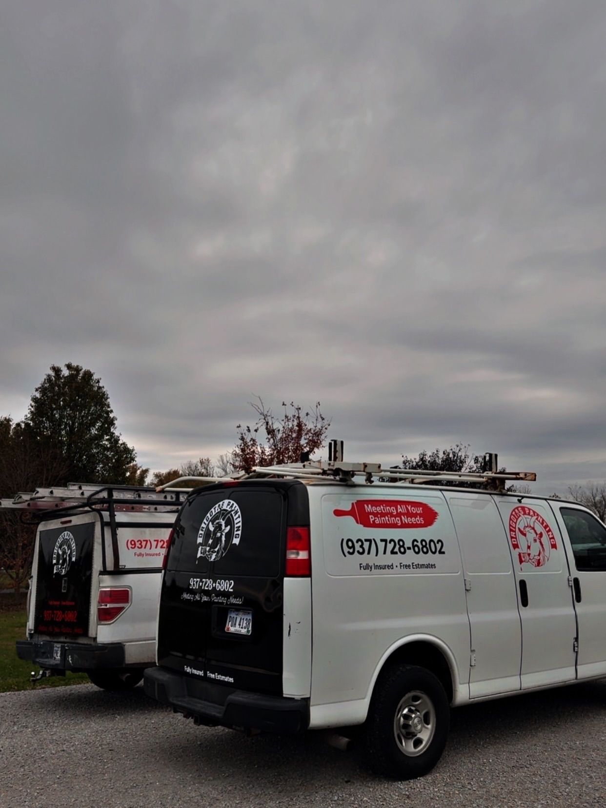 Two white vans parked outside with company logos on them under a cloudy sky.