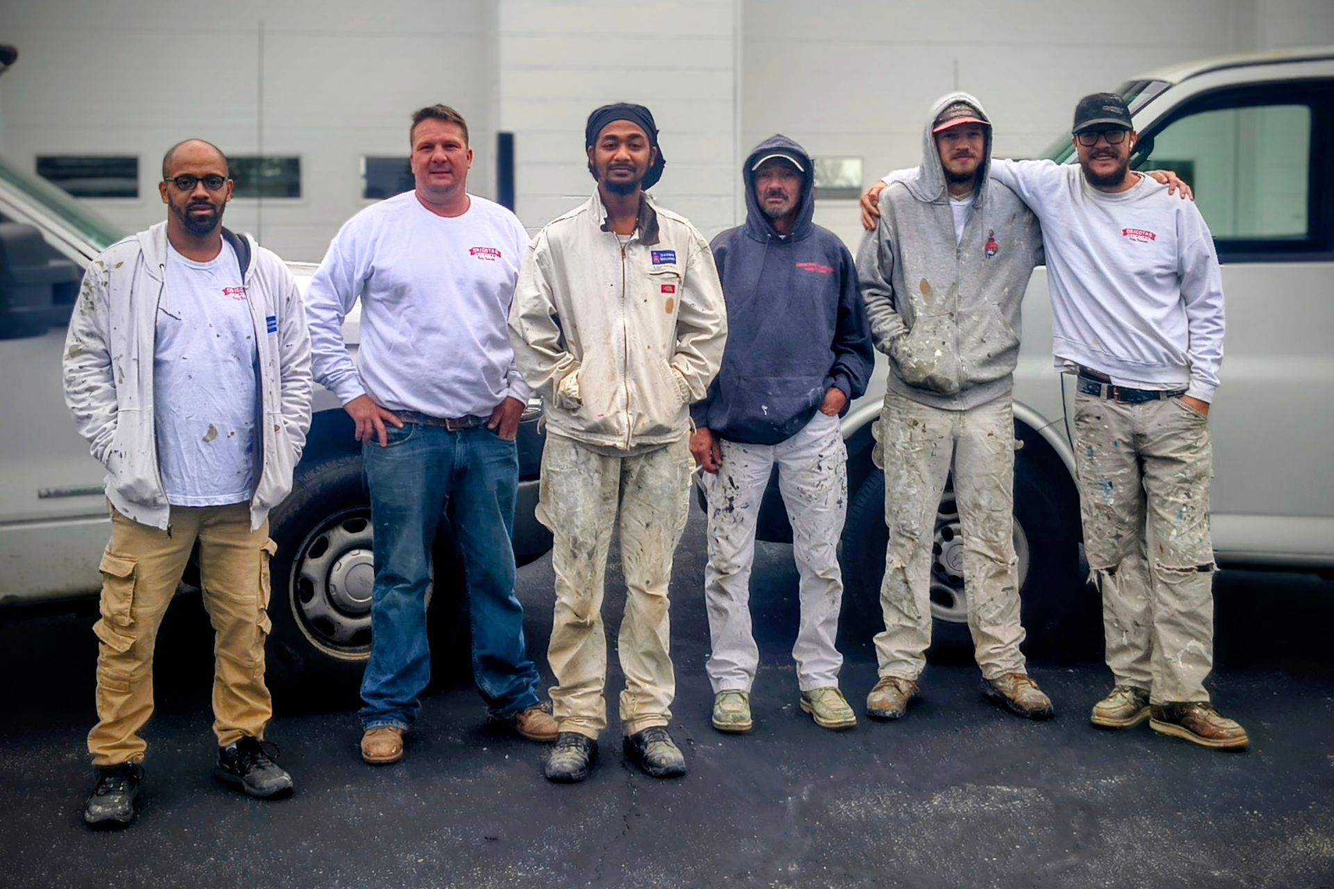 Six people in work clothes stand side-by-side in front of two white vans.