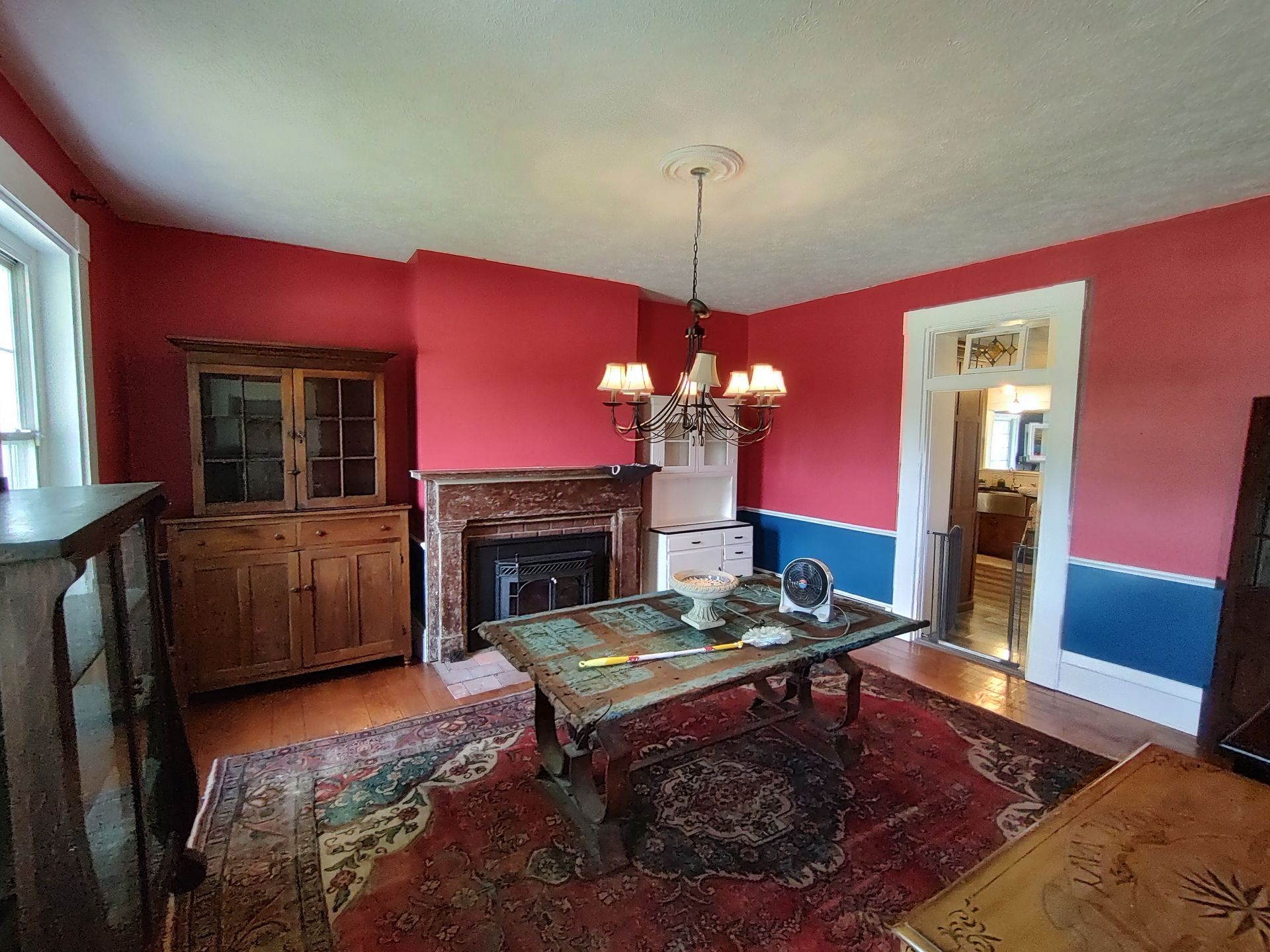 A formal dining room features red walls with a blue wainscot, a wooden hutch, a stone fireplace, and a large dining table.