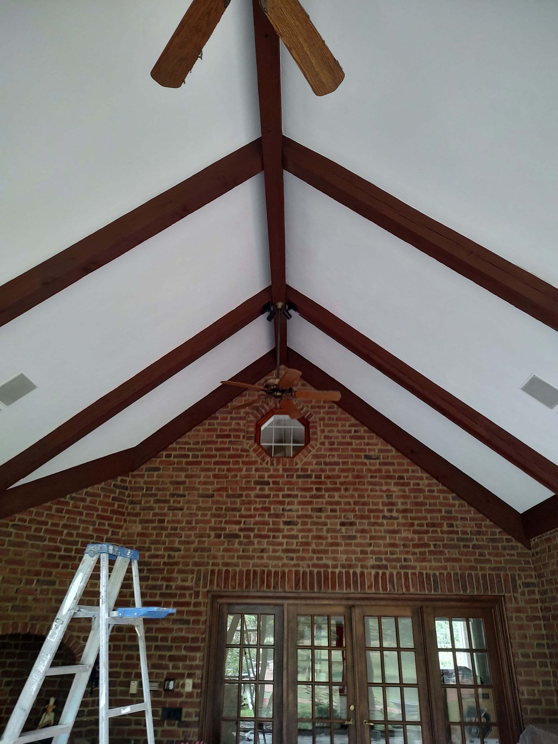 A high, vaulted white ceiling with brown wooden beams, a ceiling fan, and a brick wall with a central window and doors.