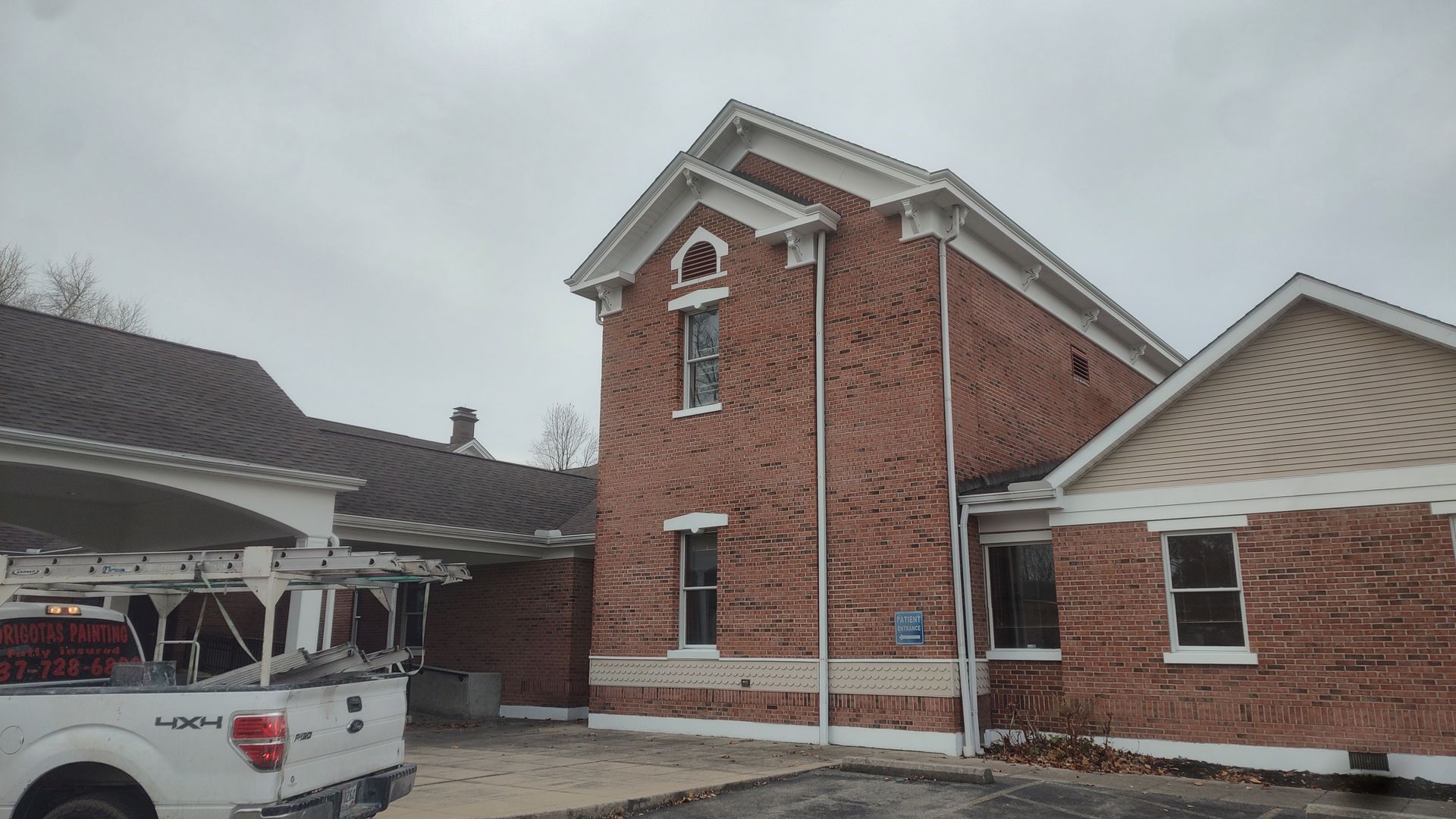 A multi-story brick building with a white gabled roof and a work truck parked in front under a covered entrance.