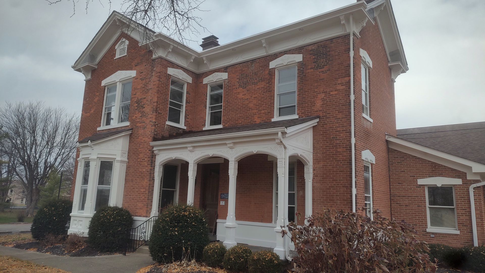 A two-story red brick house with white trim, a gabled roof, and a covered front porch, set against a cloudy sky.