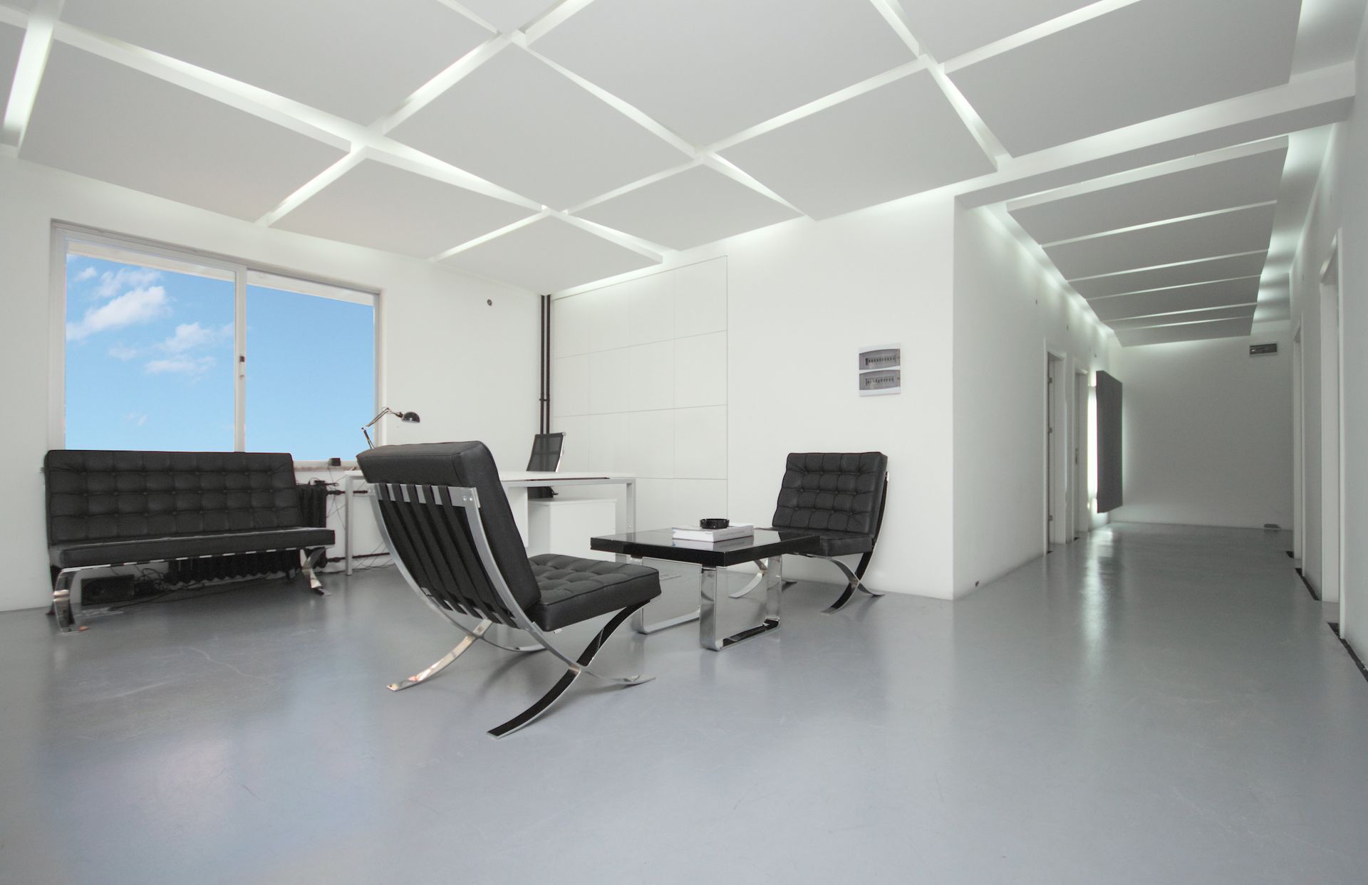 Modern office interior with black furniture, large windows, and geometric ceiling lights.