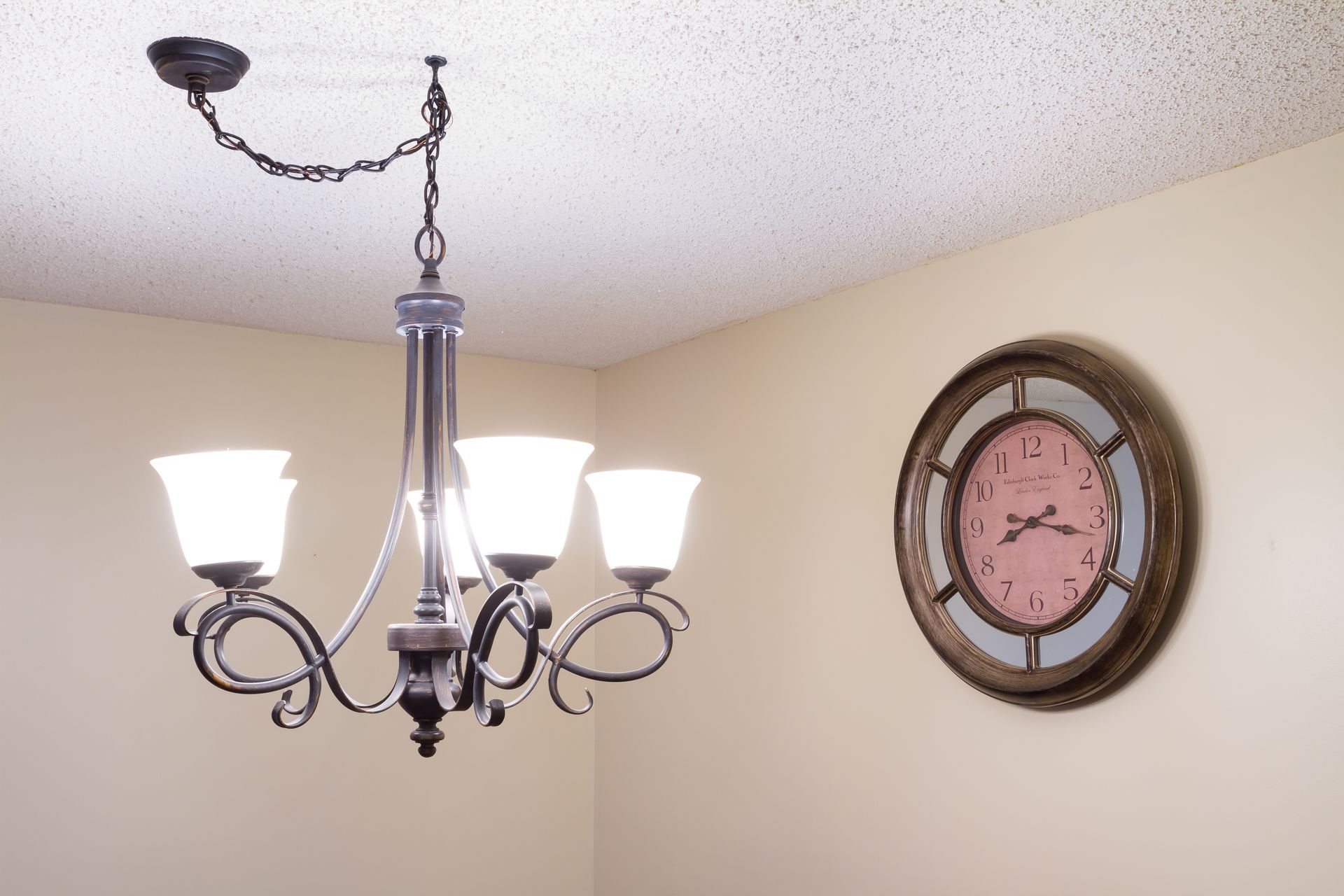 Chandelier with lit lamps hanging from the ceiling, next to a large round clock on a wall.