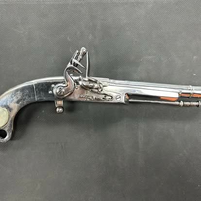 Silver flintlock pistol on a dark surface, showcasing intricate metalwork.