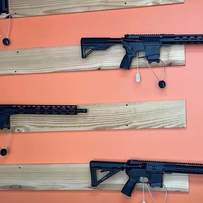 Black rifles displayed on wooden shelves against an orange wall.