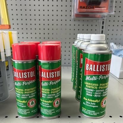 Ballistol multi-purpose lubricant spray cans with red caps and green labels. In a store setting.