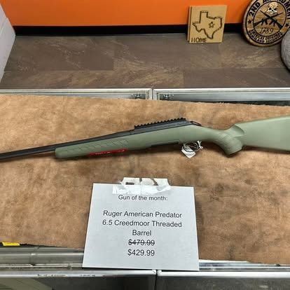 Ruger American Predator rifle with price tag on display at a gun store. Green stock, black barrel.