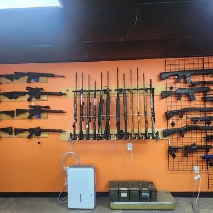 Firearms displayed on orange wall with black shelves and containers.