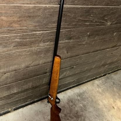 A long wooden rifle with a black barrel is leaning against a wooden wall.