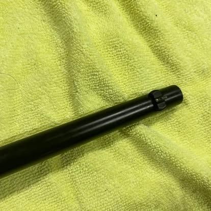 Black, cylindrical firearm barrel, possibly a rifle, on a yellow cloth background.