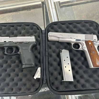 Two handguns in open cases, one black and one silver, on a reflective surface.