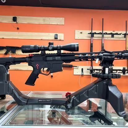 A black rifle with a scope, mounted on a stand, displayed in a gun shop.