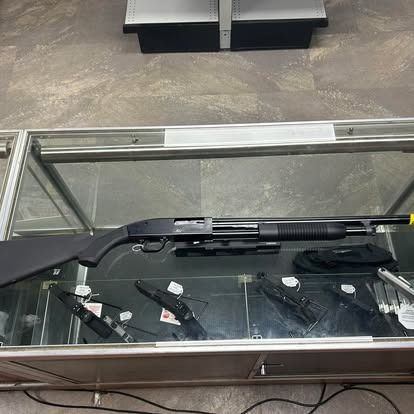 Shotgun in a glass display case with knives and accessories.