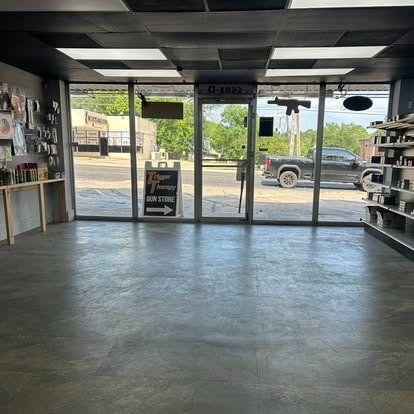 Empty retail shop interior, glass storefront. Concrete floor, shelves, a sign and a vehicle outside.