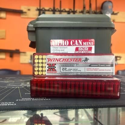 Ammo can, Winchester .22 LR ammunition box, and red cartridge case on a table.