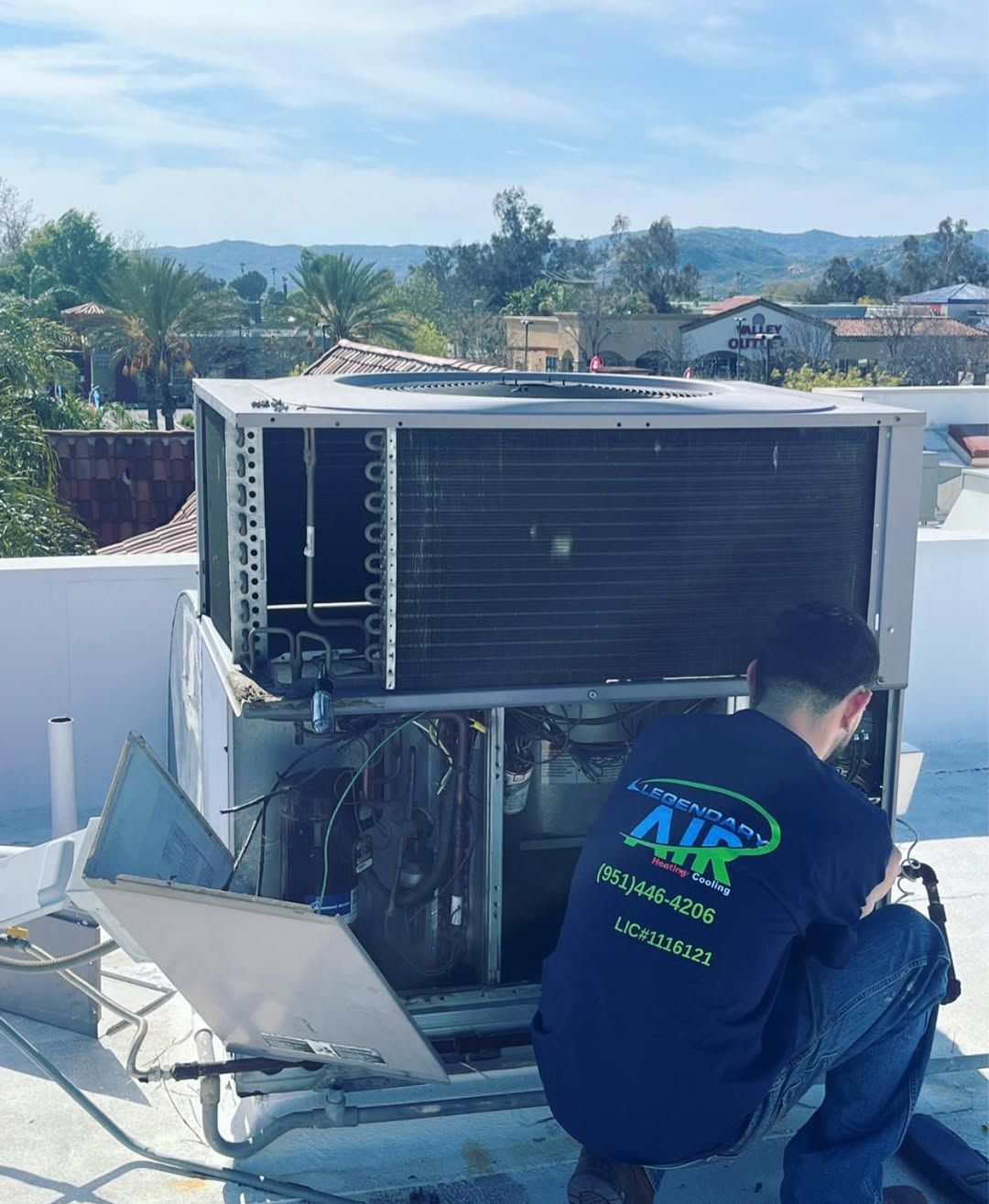 A man is working on an air conditioner on a roof.