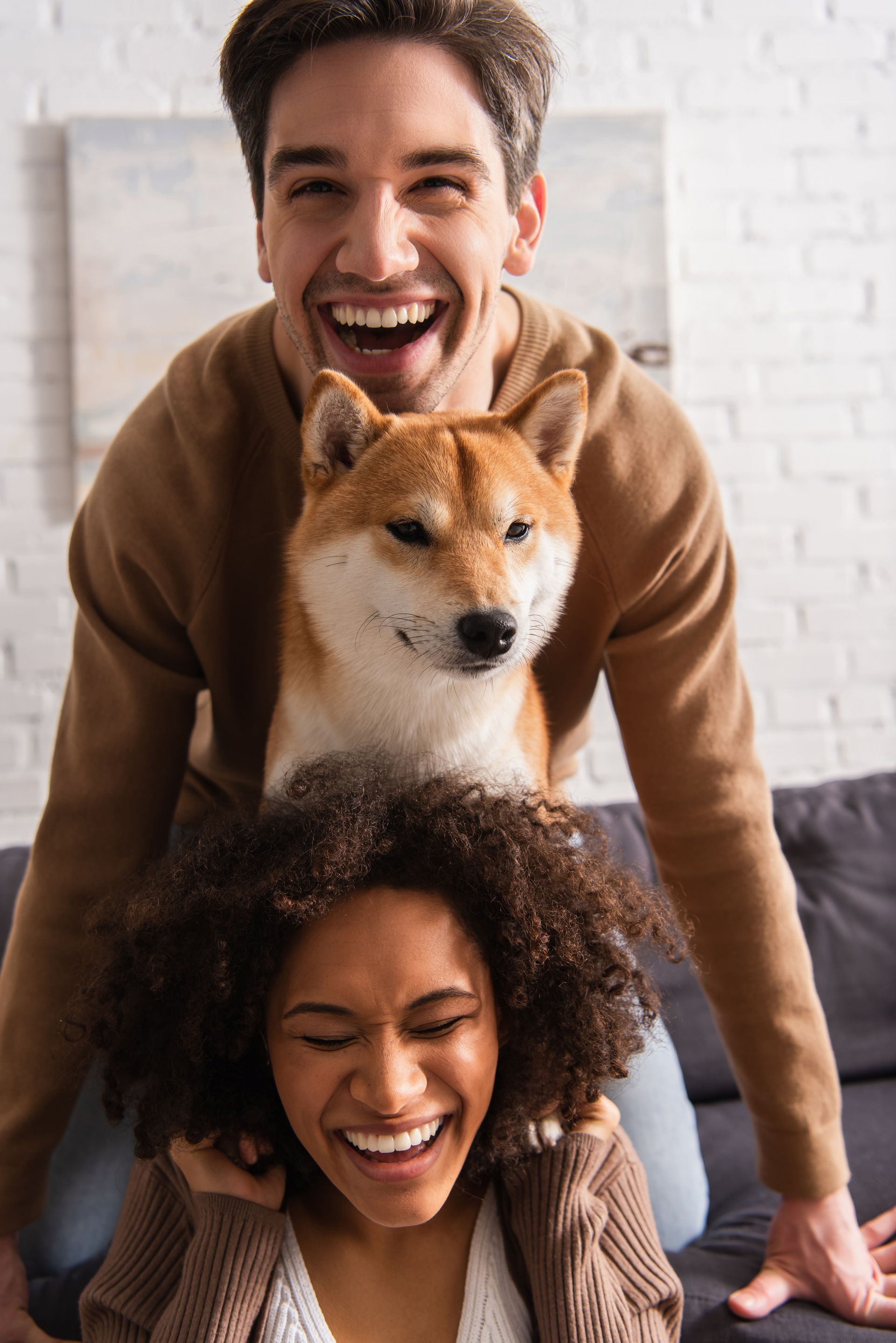 A man is giving a woman a piggyback ride with a dog on her head.