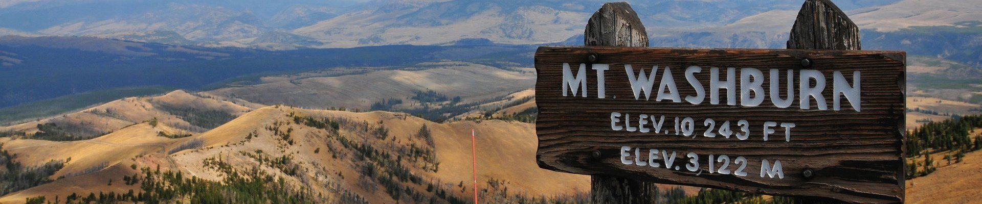 Weathered wooden Mount Washburn sign with the scenic landscape of the Yellowstone northern range in the background