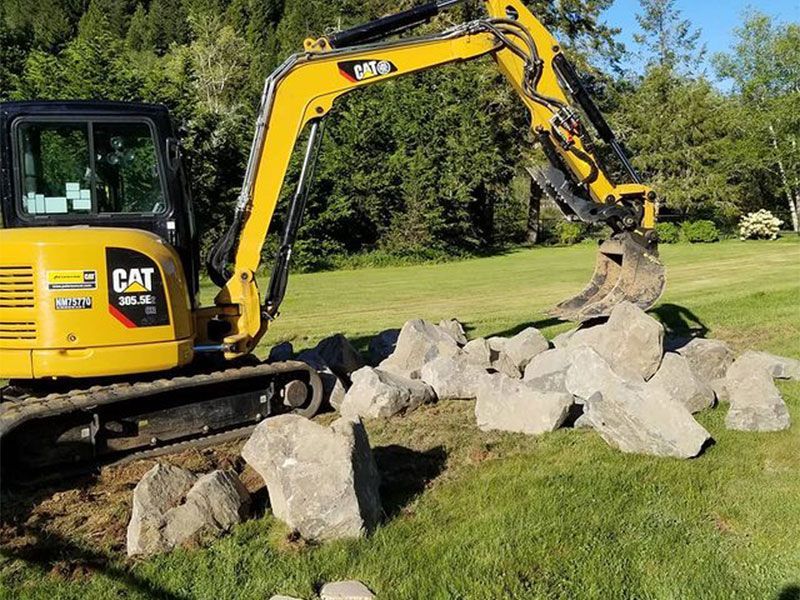 A yellow cat excavator is working on a pile of rocks.