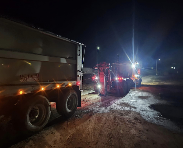 A dump truck is being towed by a bulldozer at night.