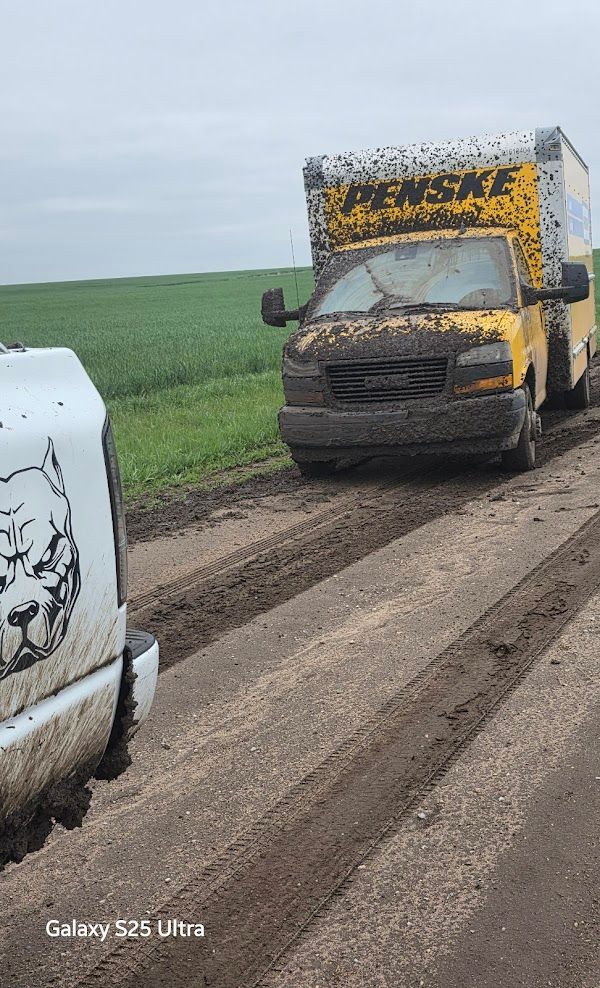A muddy truck is driving down a dirt road next to a white truck.