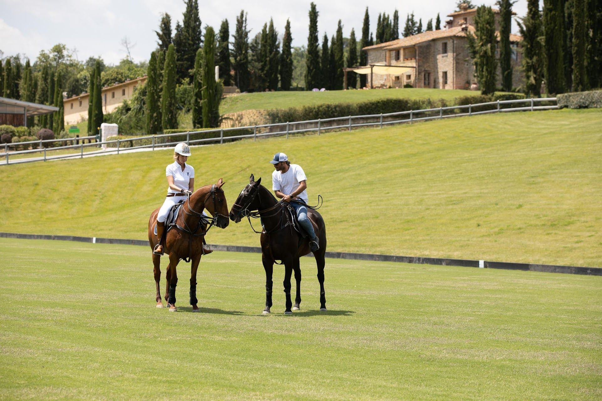 Two people riding horses on a field with a house in the background