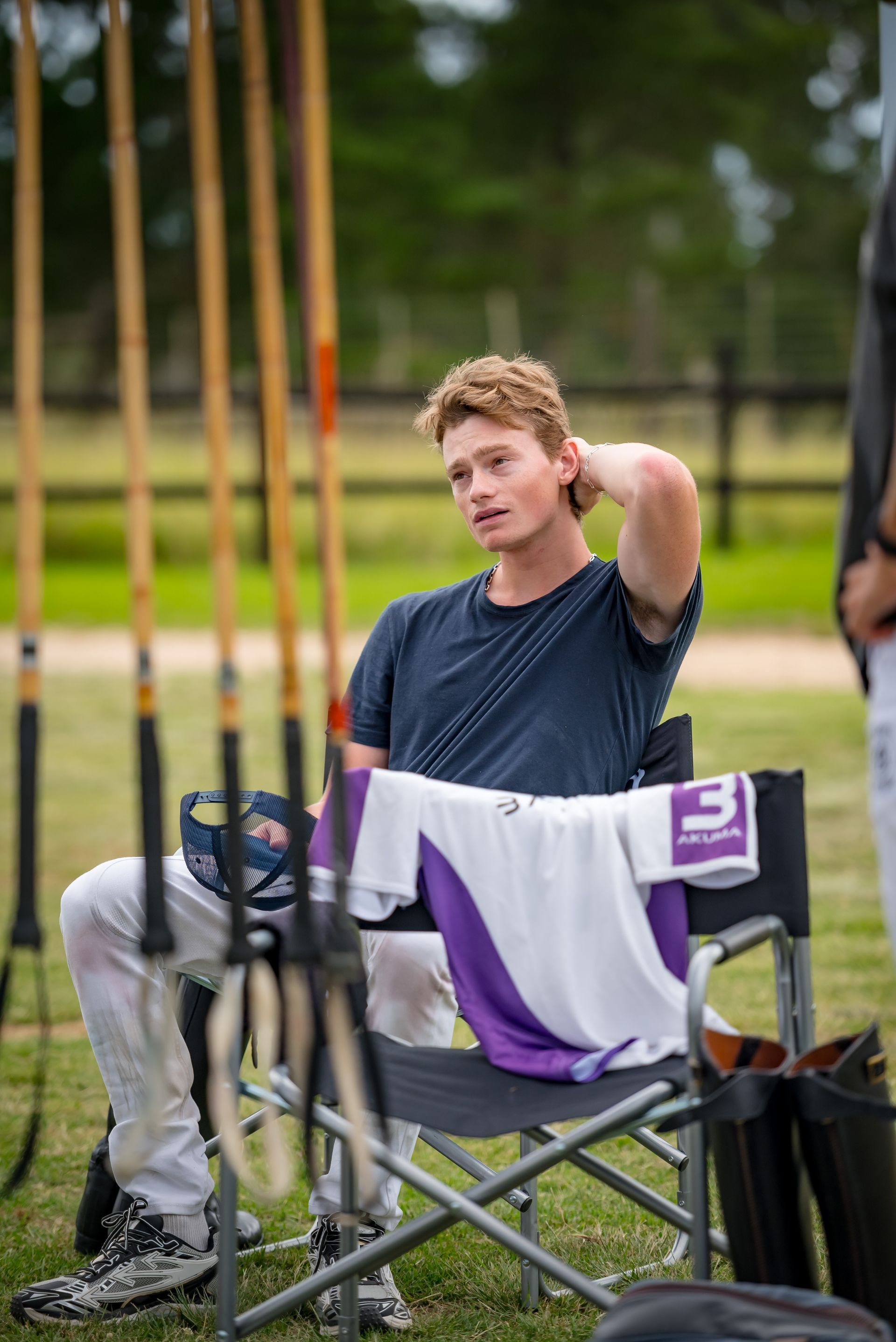 A young man is sitting in a folding chair in a field.
