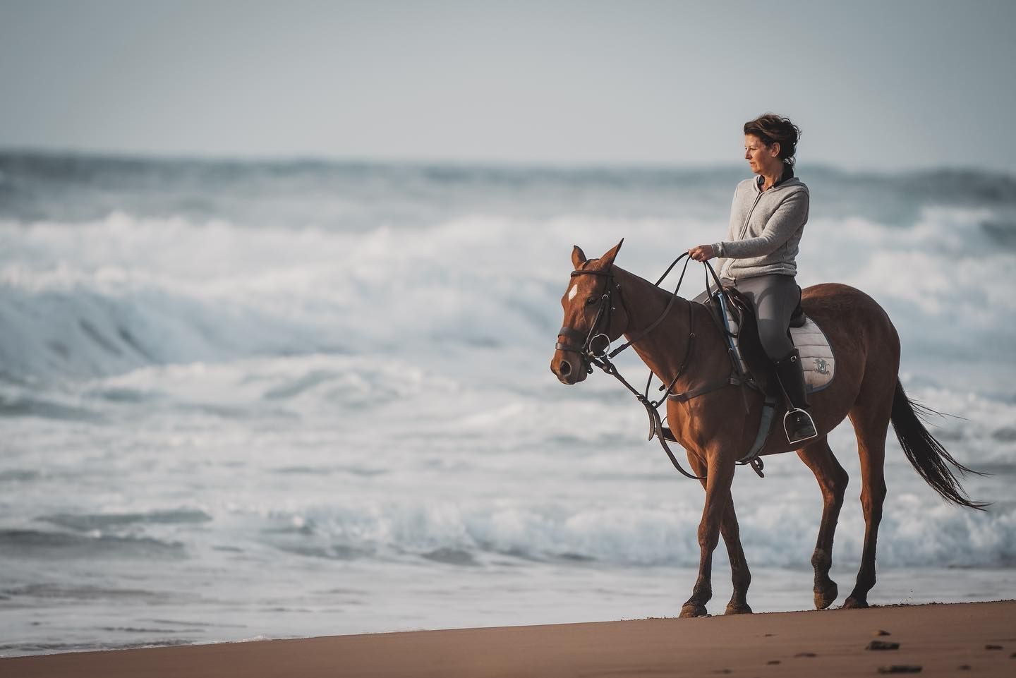 A woman is riding a horse on the beach near the ocean.