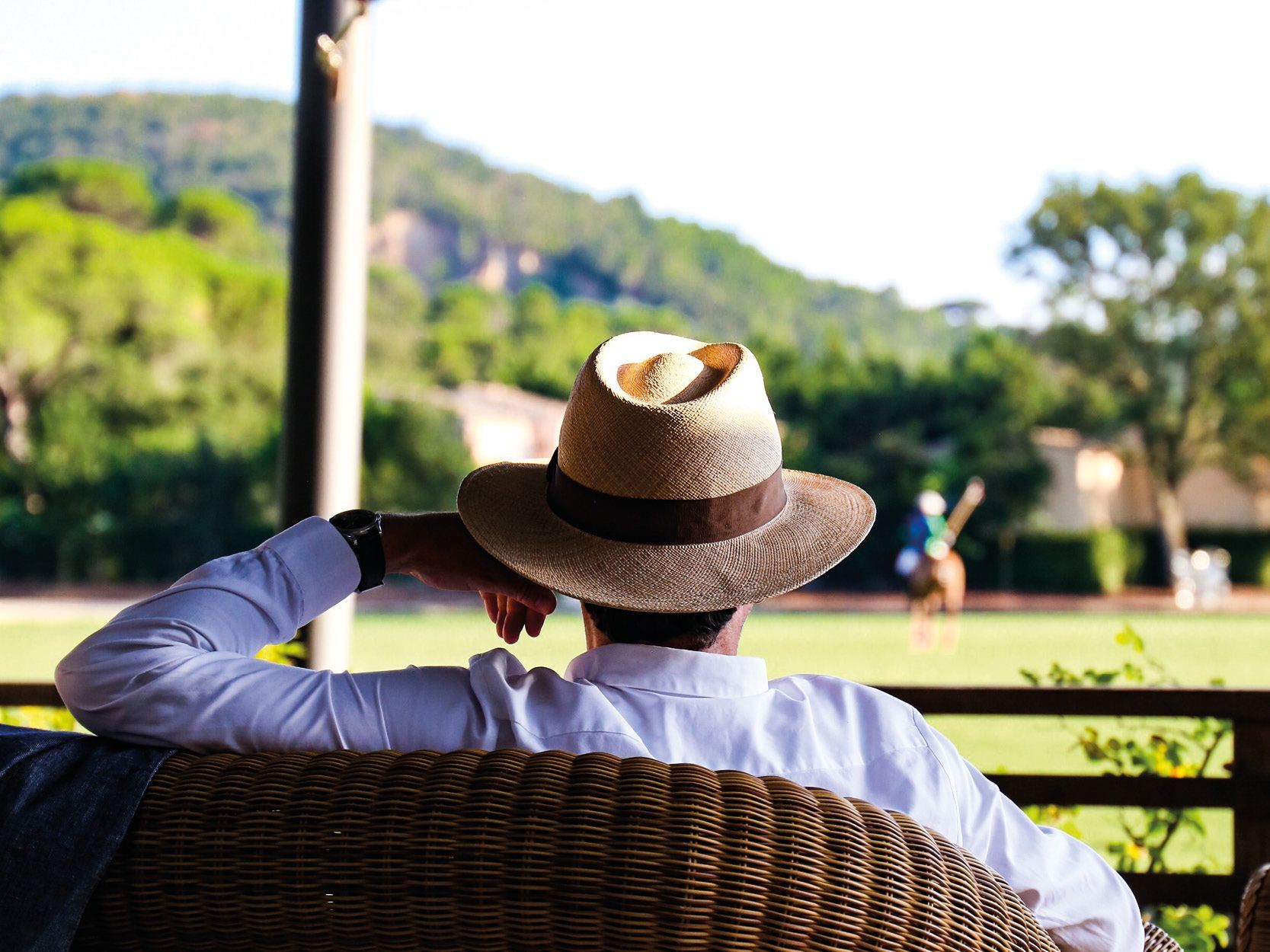 A man wearing a hat is sitting in a chair looking at a field.